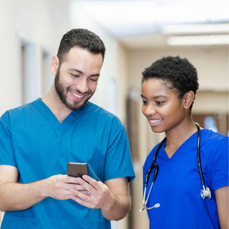 Smiling male nurse in light blue scrubs, holding a phone and showing a smiling female nurse in dark blue scrubs